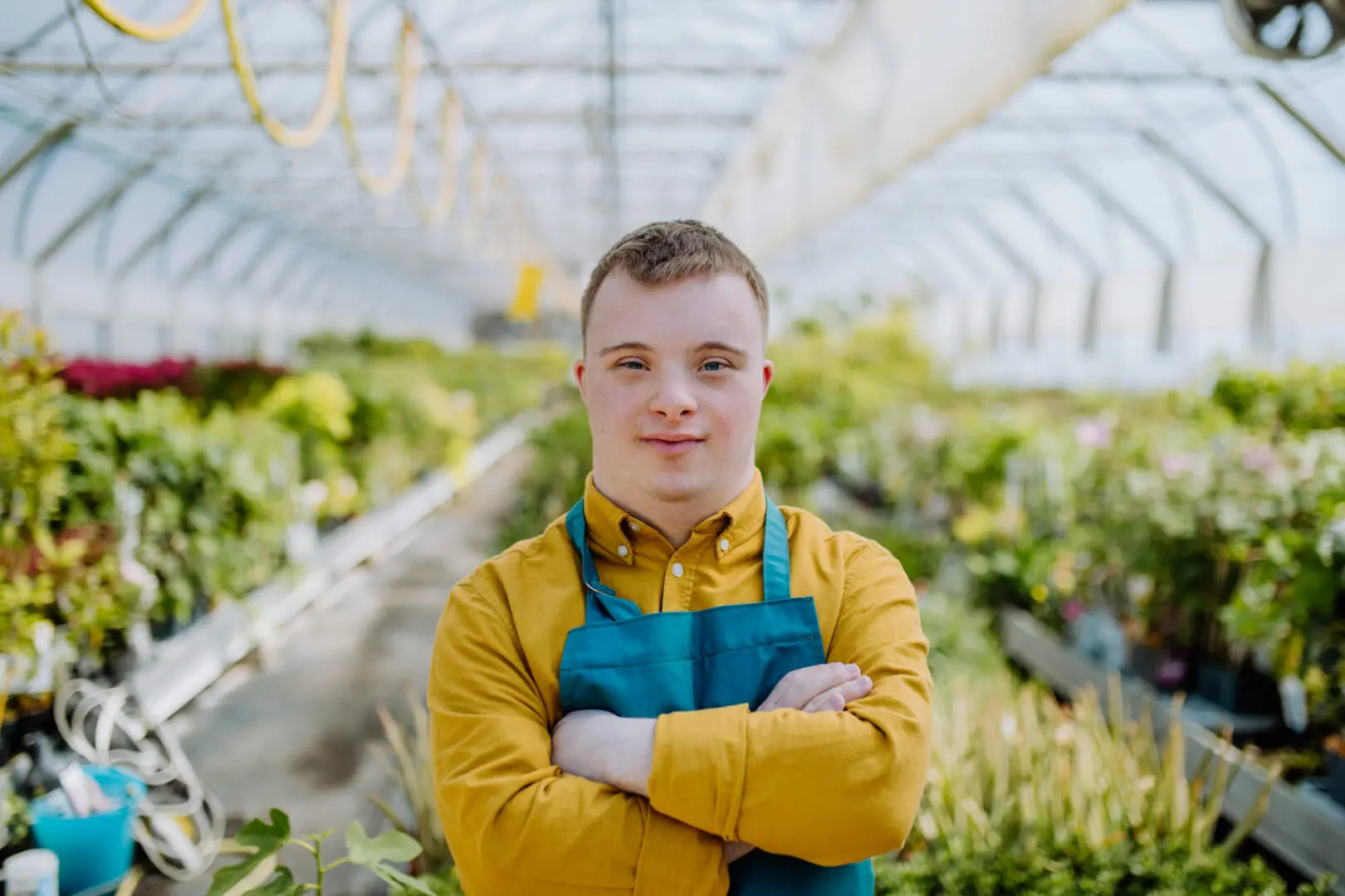 Young gardener confidently standing in a greenhouse with arms crossed.