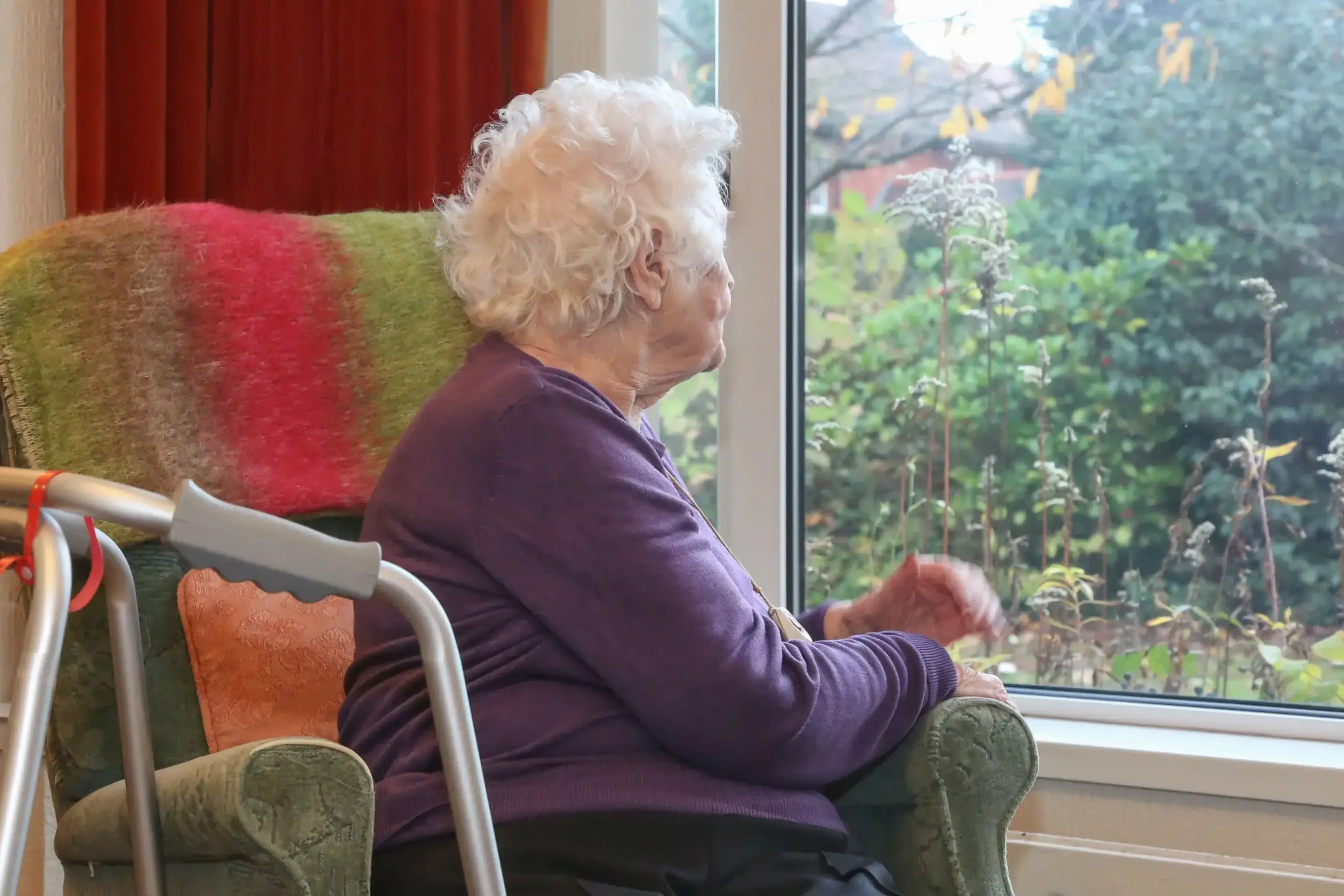 Elderly woman in wheelchair looking thoughtfully out a window.